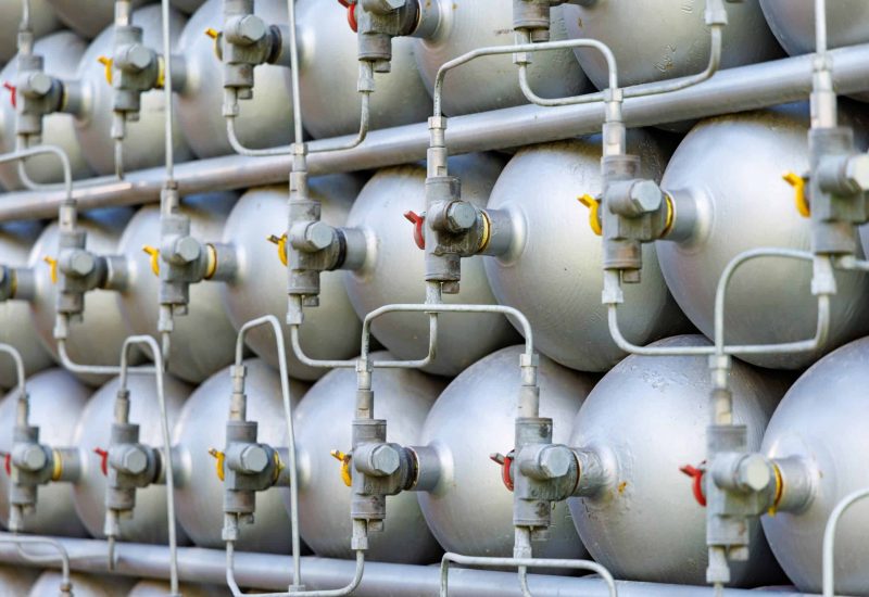 A lot of different small metal bottles filled with gas or gasoline are stacked in large piles and illuminated by the bright warm daytime sun