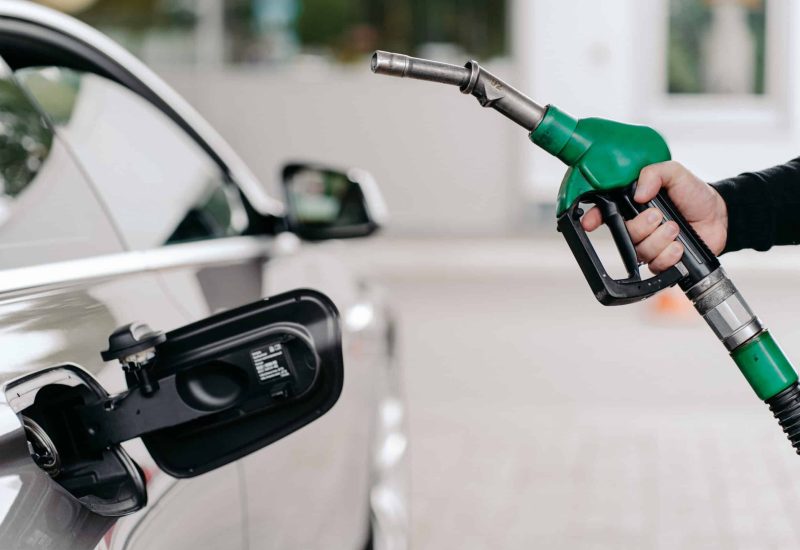 Cropped shot of mans hand pumping gasoline fuel in car at gas station. Auto being filled with petrol. Unrecognizable man holds fuel nozzel.