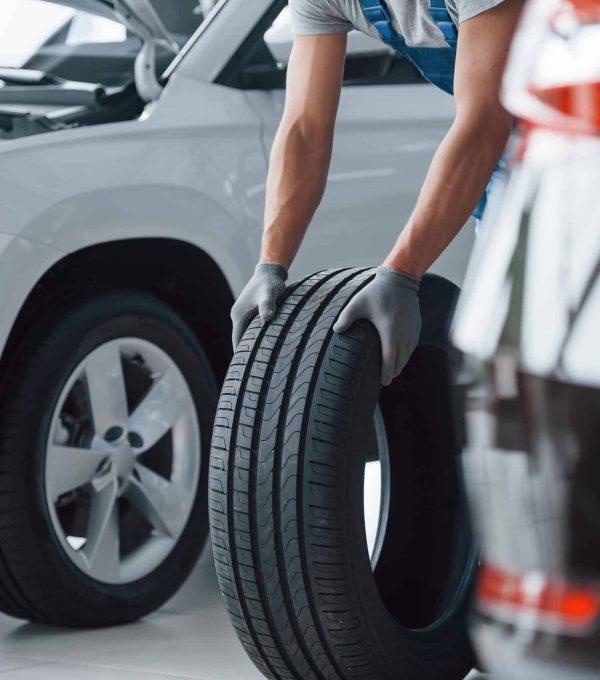 White and black cars. Mechanic holding a tire at the repair garage. Replacement of winter and summer tires.