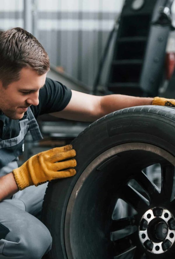 Replacement of the old tire. Man in uniform is working in the auto service.